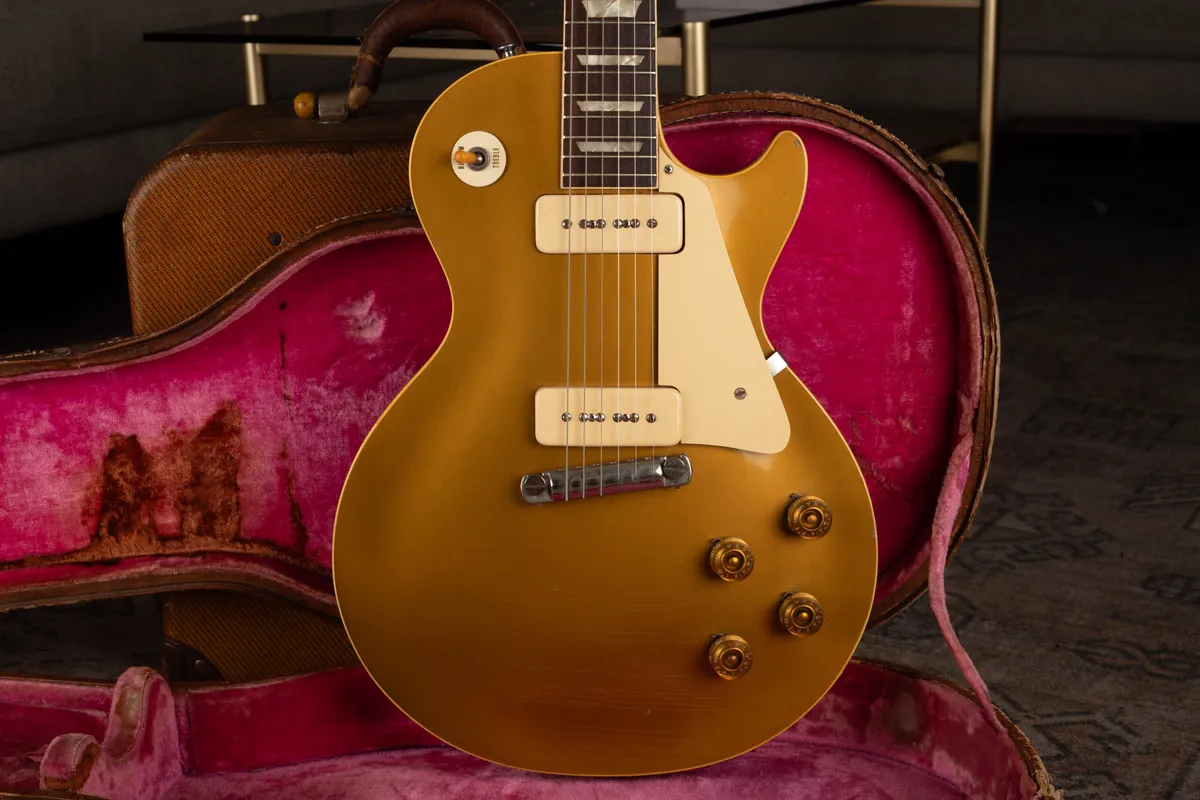 A 1954 Gibson Les Paul Goldtop with cream P-90 pickups and a cream pickguard, resting upright in its original brown hardshell case with worn pink lining.