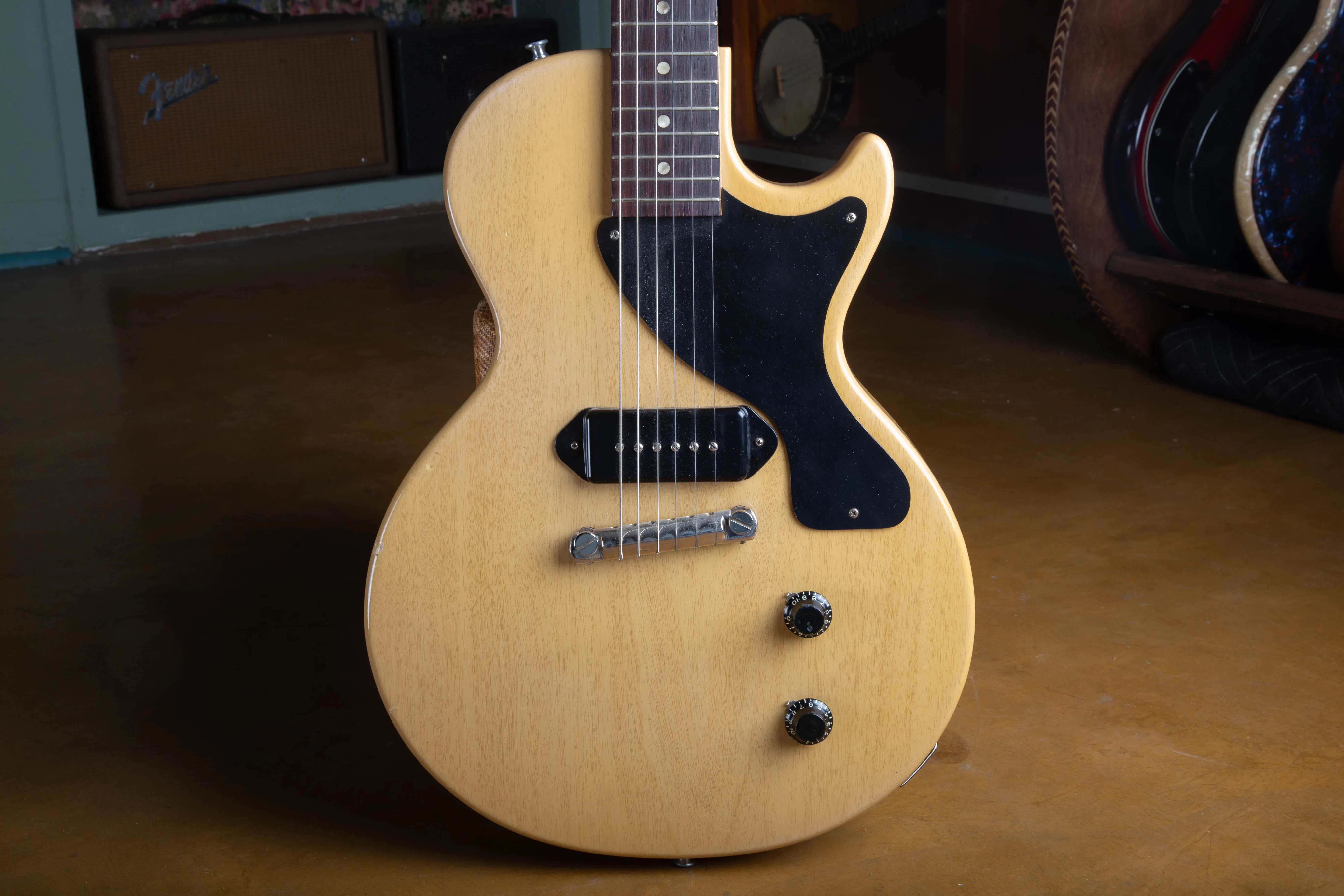 Close-up of the front of a 1957 Gibson Les Paul TV Model body, showing the single black dog-ear P-90 pickup, the single-ply black pickguard, the one-piece wraparound bridge, and two black bonnet knobs against the limed mahogany finish.
