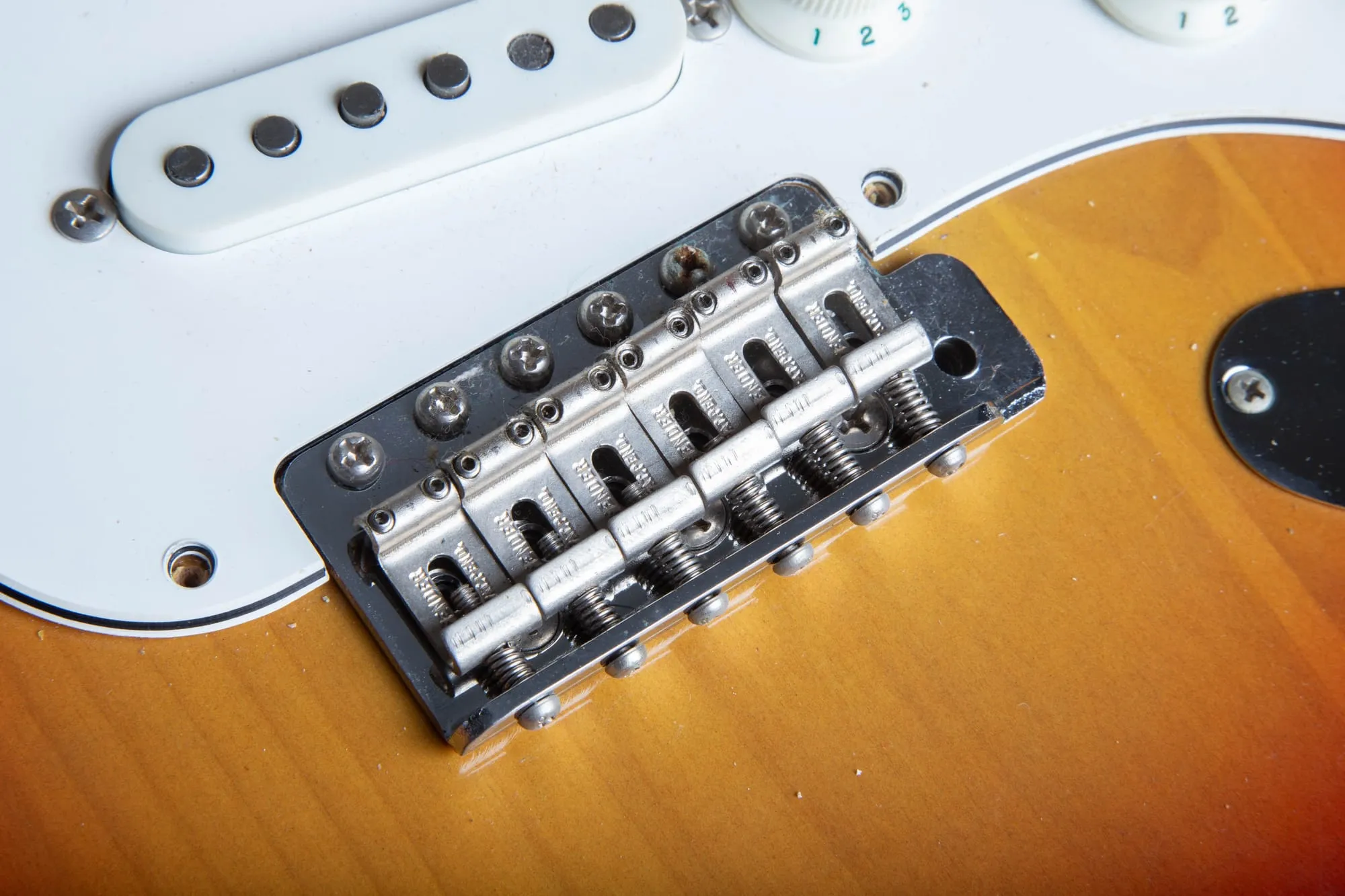 Steel tremolo bridge saddles on a 1967 Fender Stratocaster, each stamped FENDER PAT. PEND., with the steel tremolo block and springs visible below on a sunburst body.