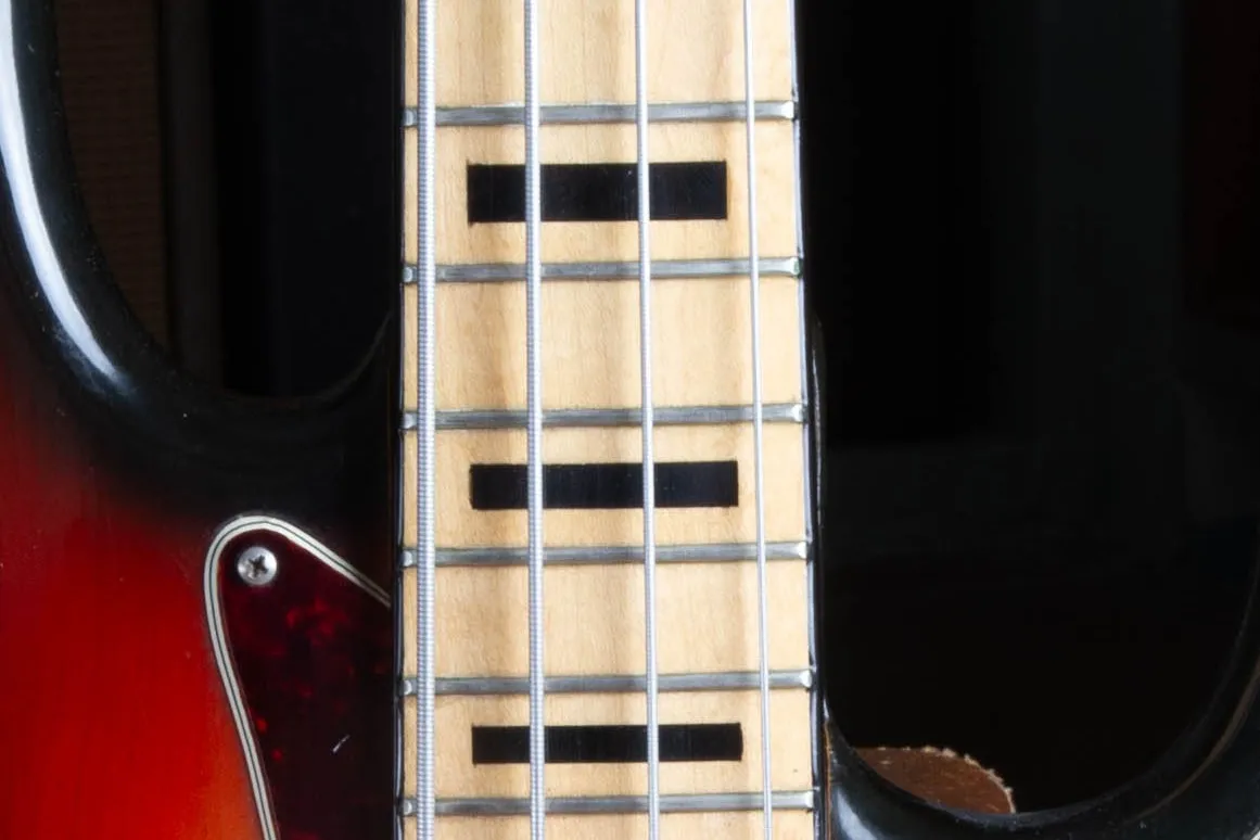 Close-up of the 1973 Fender Jazz Bass maple fingerboard showing white binding, bold black block inlays, and the warm amber tone the maple has developed under the lacquer
