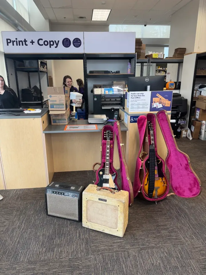 Two Gibson guitars and two vintage amplifiers at a FedEx counter for packing and insured shipping