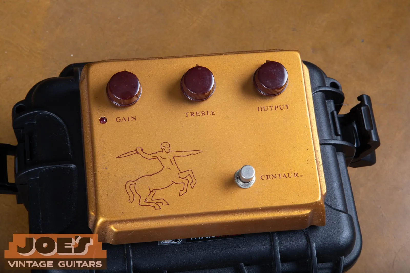 The gold top face of an original Klon Centaur professional overdrive, showing three oxblood knobs marked Gain, Treble, and Output, a red LED, the red centaur archer graphic, and the footswitch.